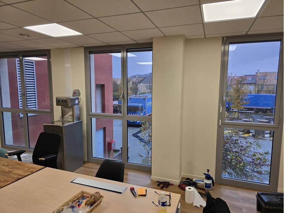 Pose en cours de film solaire dans des bureaux IDF — fenêtres teintées bleues, outils de pose visibles sur la table, novembre 2024