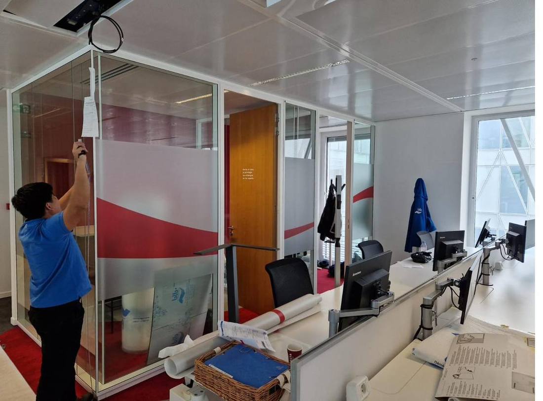 Technicien DFP France posant un film décoratif blanc et rouge sur une cloison vitrée en open space professionnel